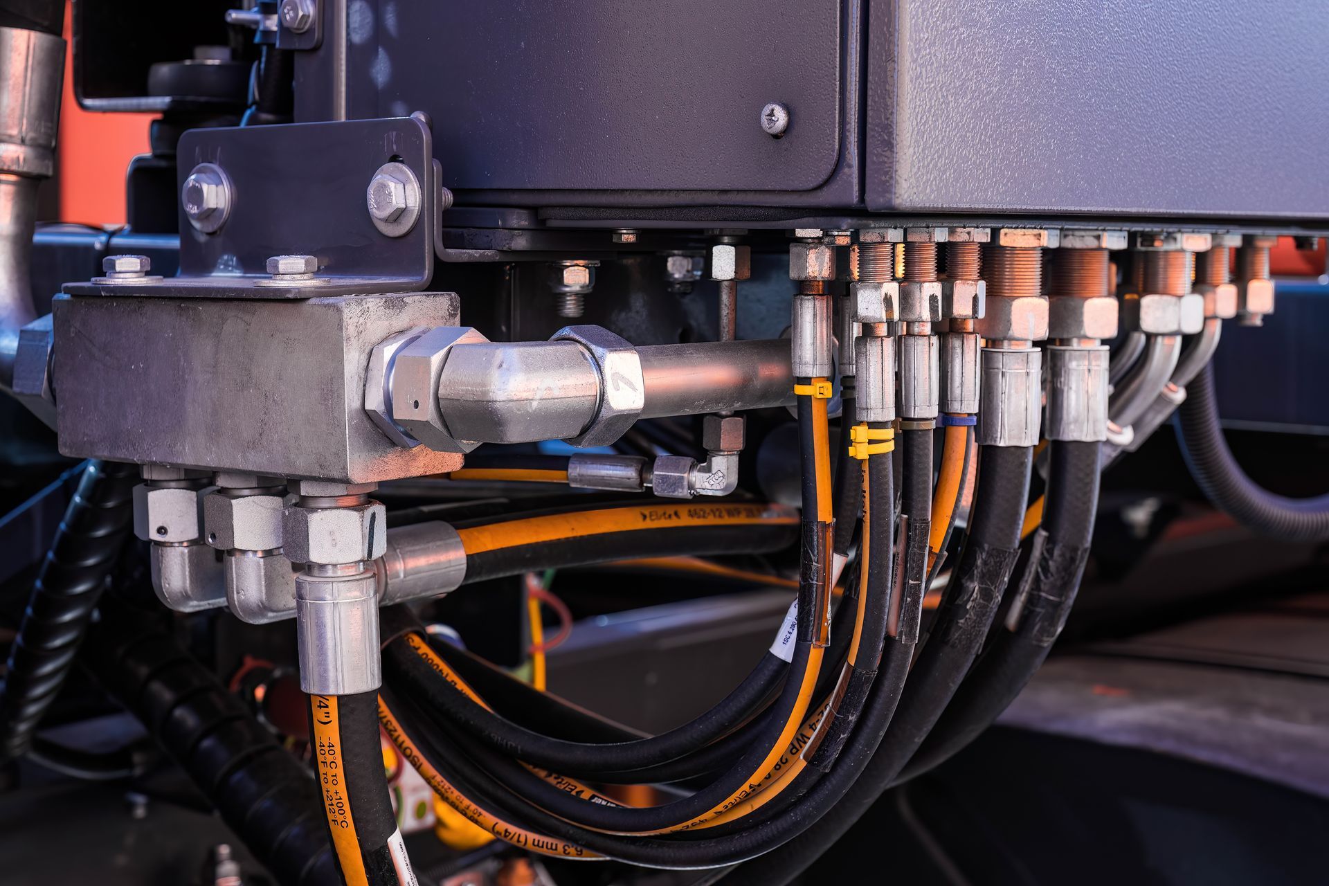 Close-up of hydraulic manifold block connected to multiple black and yellow high-pressure hoses on heavy machinery.