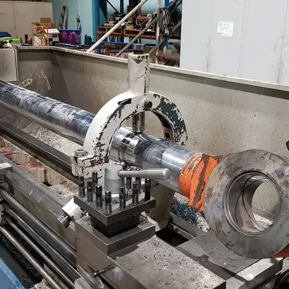 A metal cylinder held by a steady rest on an industrial lathe in a workshop.