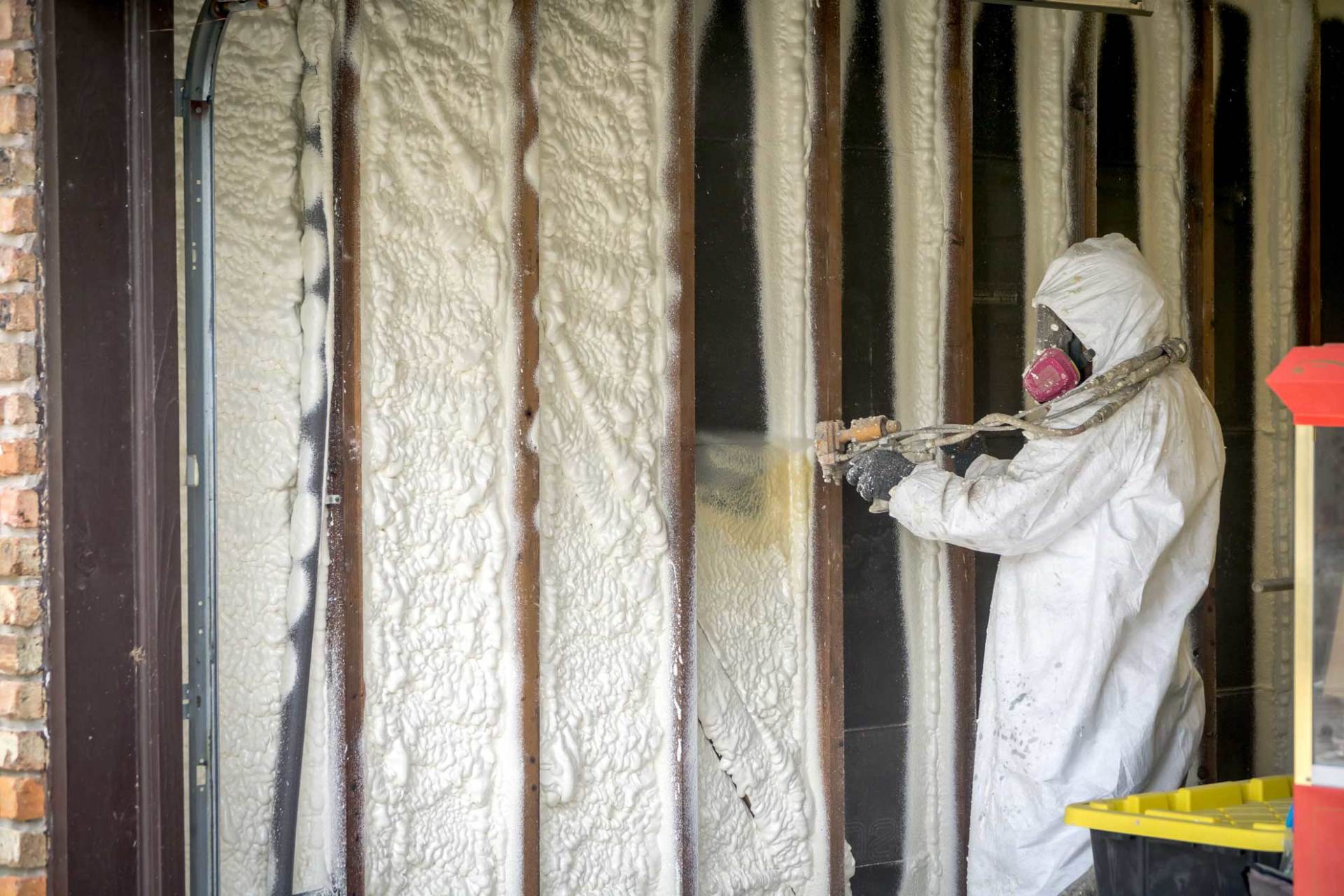 Un homme en combinaison de protection pulvérise de l'isolant sur un mur.