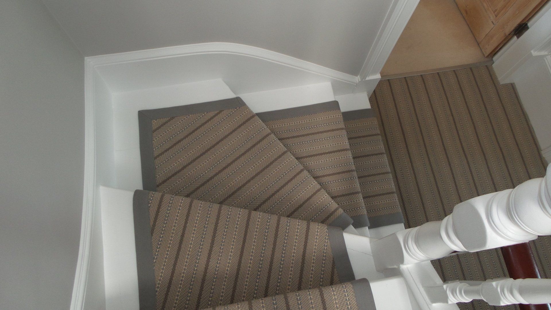 Staircase with gray and beige carpet steps, white railing, and wall.
