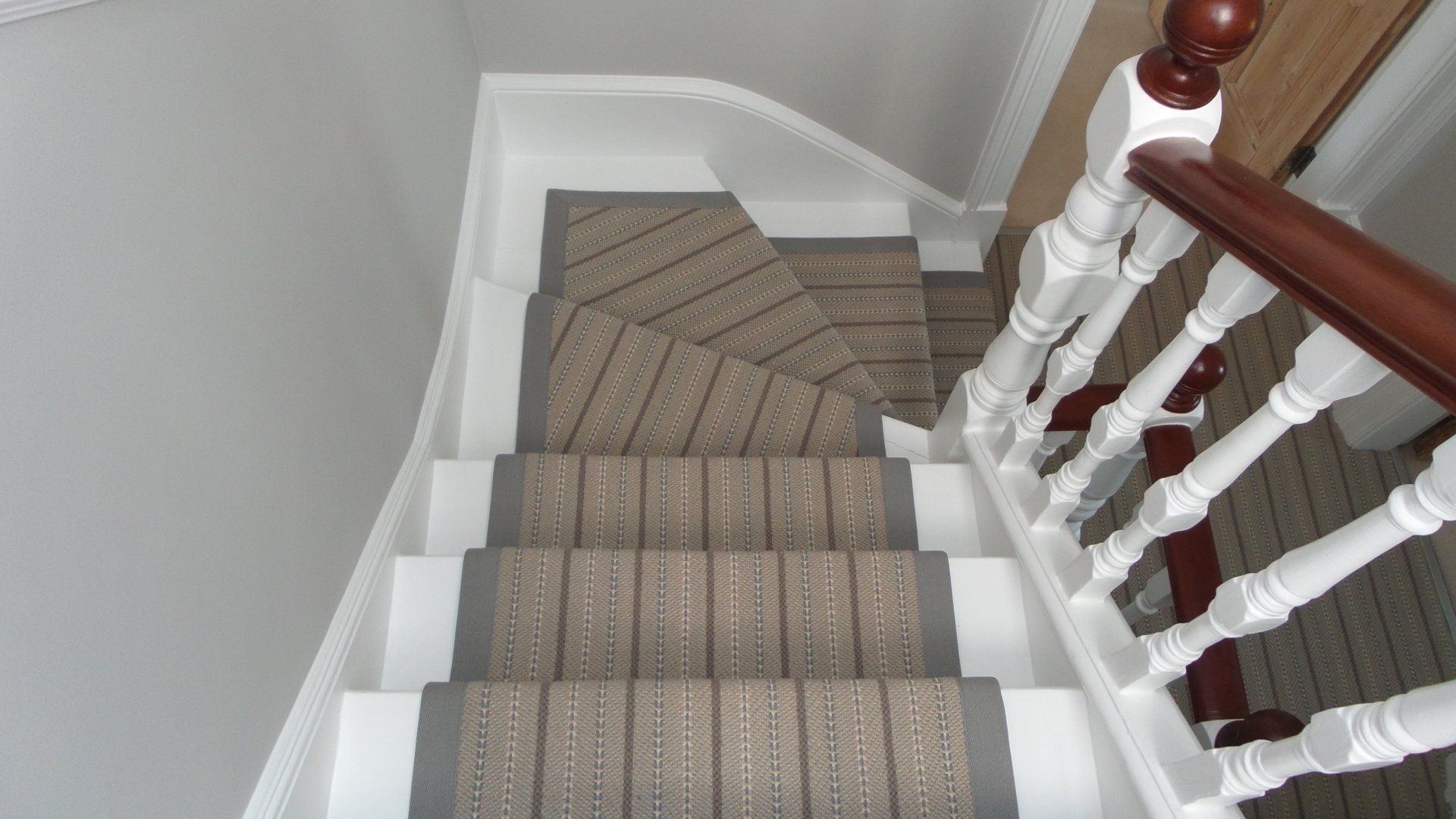 Staircase viewed from above. Beige carpeted stairs with white risers and railing, brown handrail.