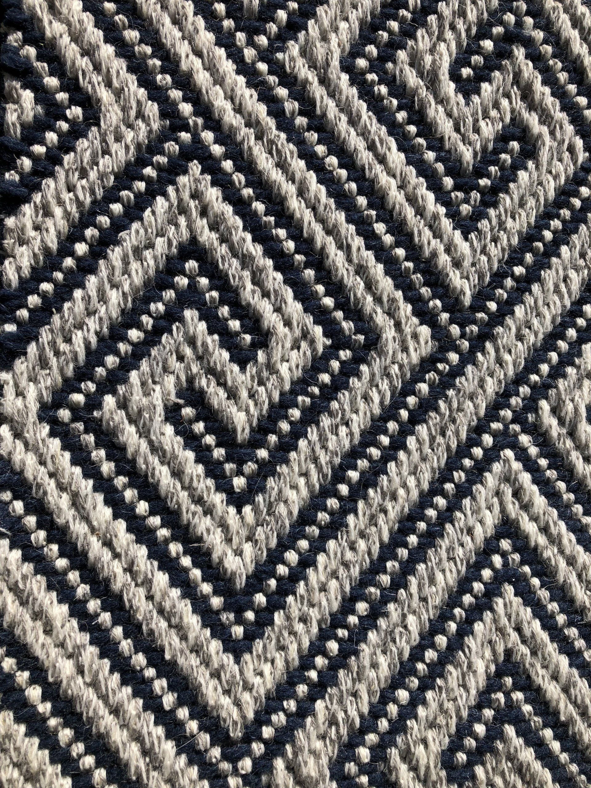 Close-up of a woven rug with a geometric pattern in dark blue and off-white.