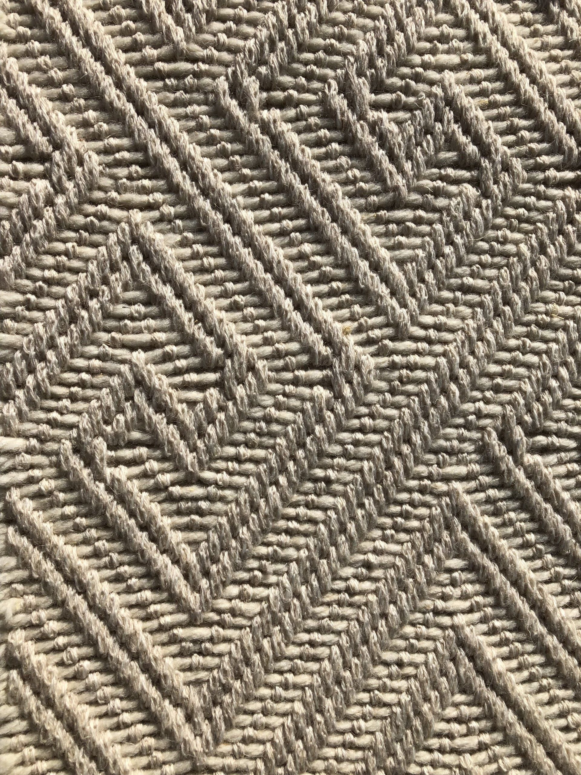 Close-up of a woven rug with a repeating geometric pattern in light beige.