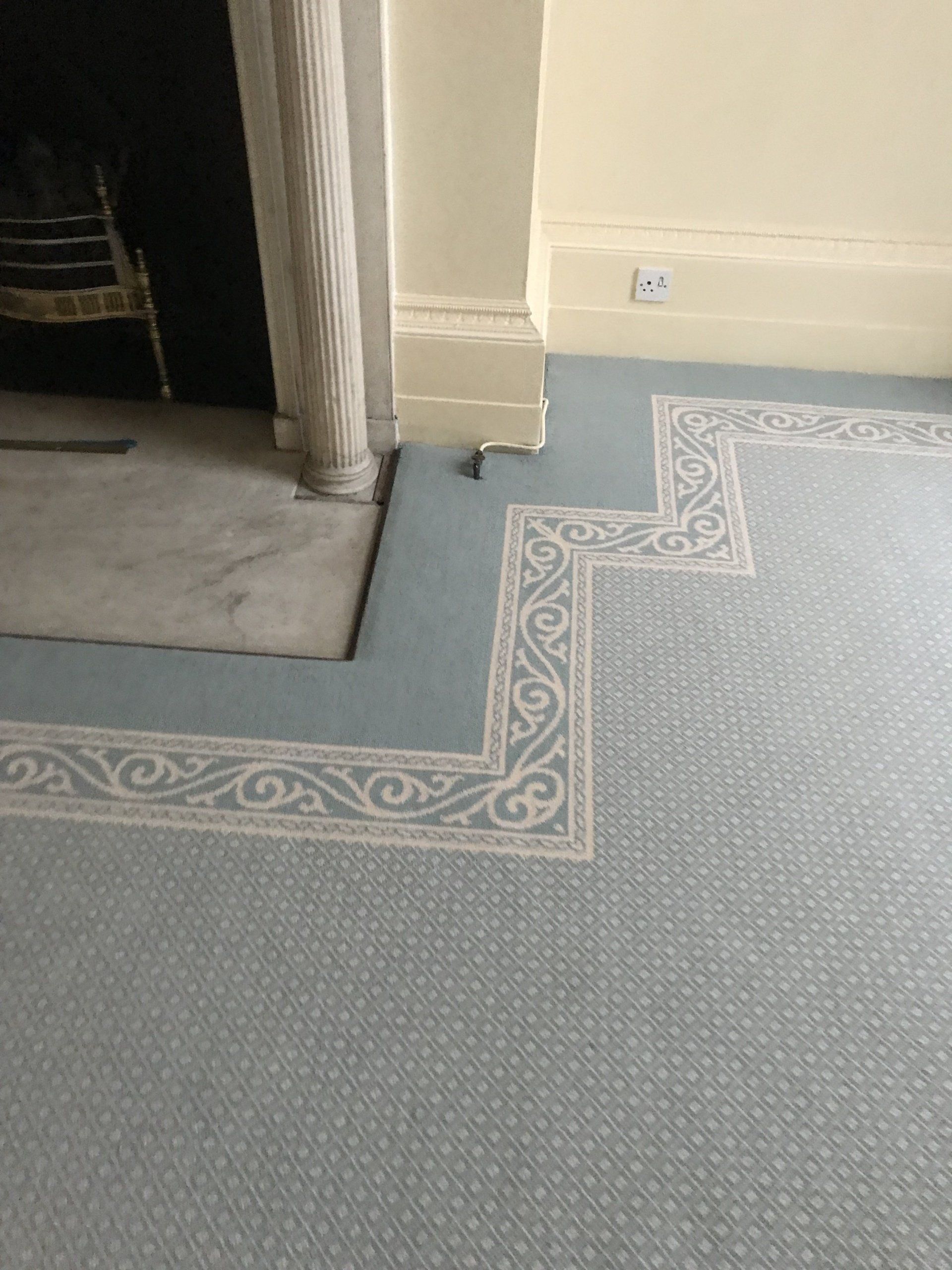 Blue carpet with decorative border framing a fireplace and wall.