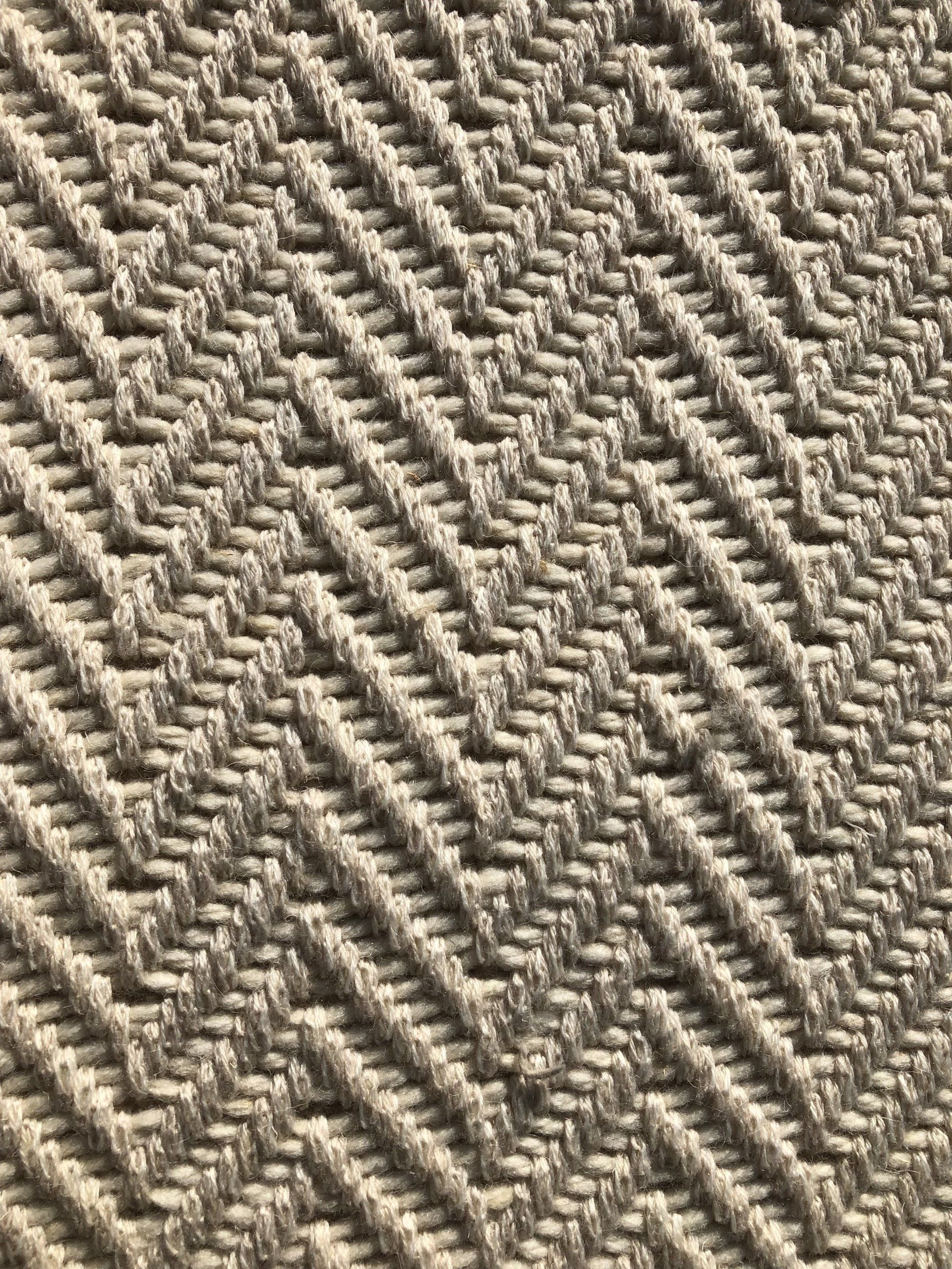 Close-up of a woven rug in a repeating herringbone pattern, in shades of beige and off-white.