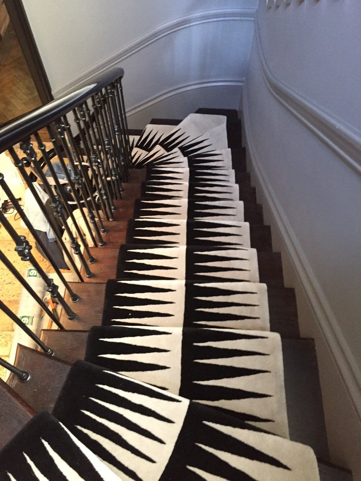 Staircase with a black and white geometric patterned runner. Wooden steps, black railing, white walls.