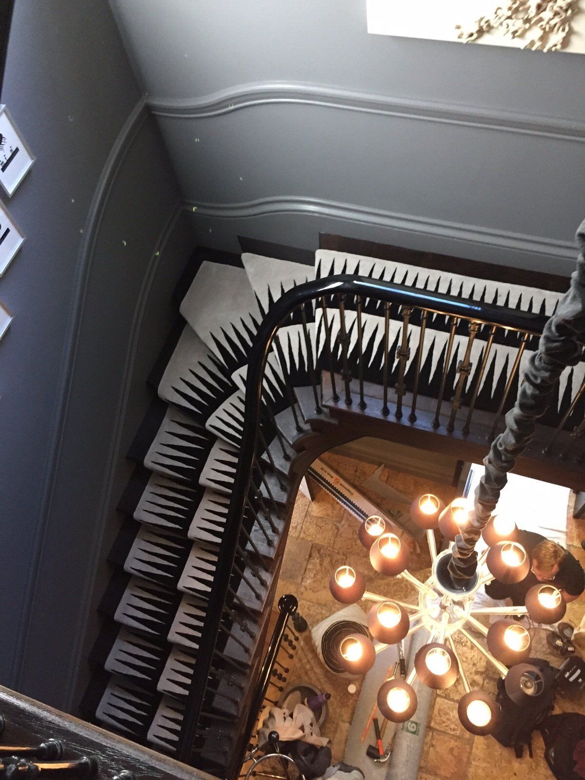 Looking down a curved staircase with black and white patterned steps and a modern chandelier.