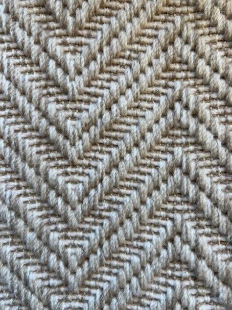 Close-up of a beige carpet with a repeating, angled chevron pattern.