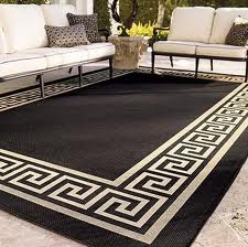 Black outdoor rug with a Greek key border under patio furniture.