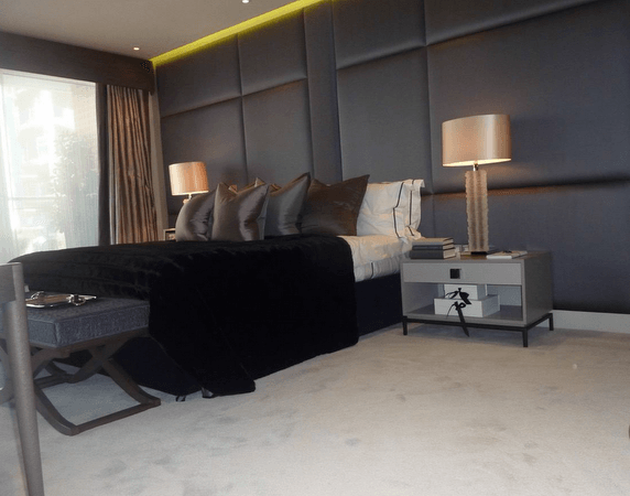 Bedroom with a large bed, dark blue upholstered wall, two bedside lamps, and grey carpet.