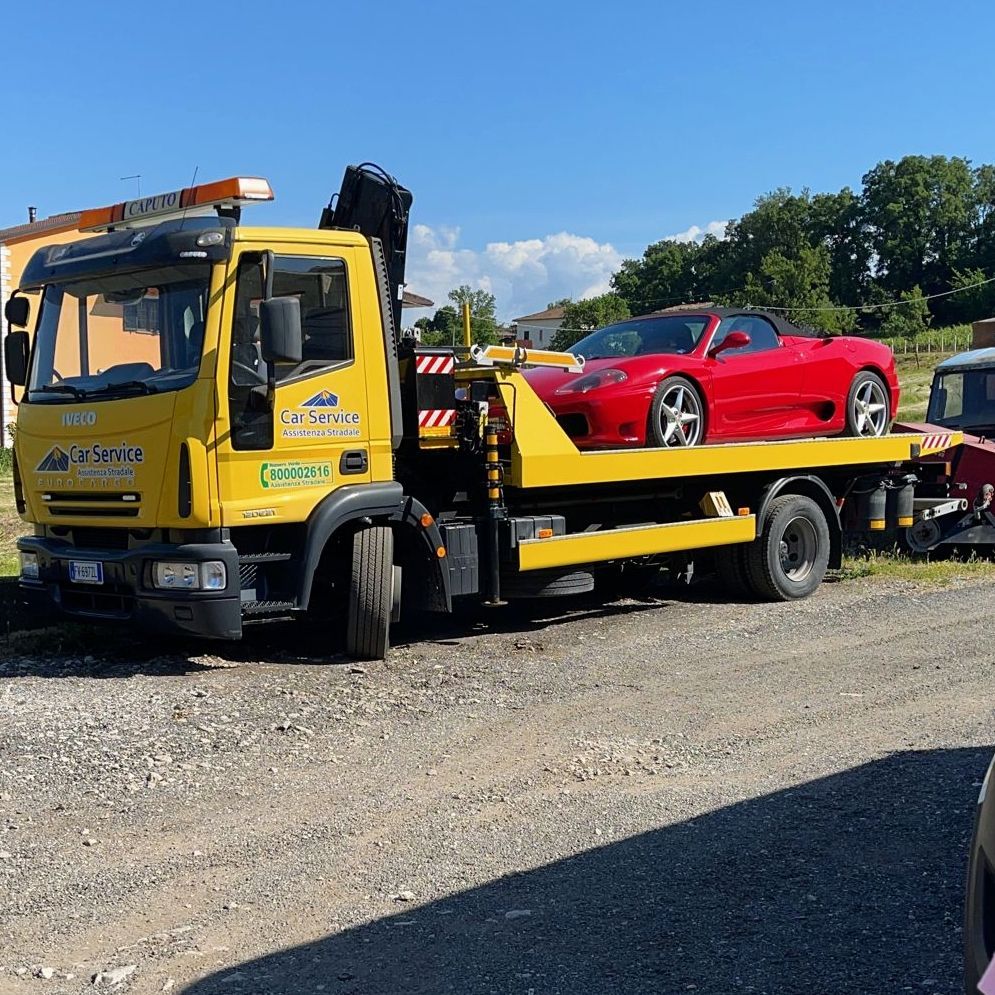 Un carro attrezzi giallo trasporta un'auto sportiva rossa