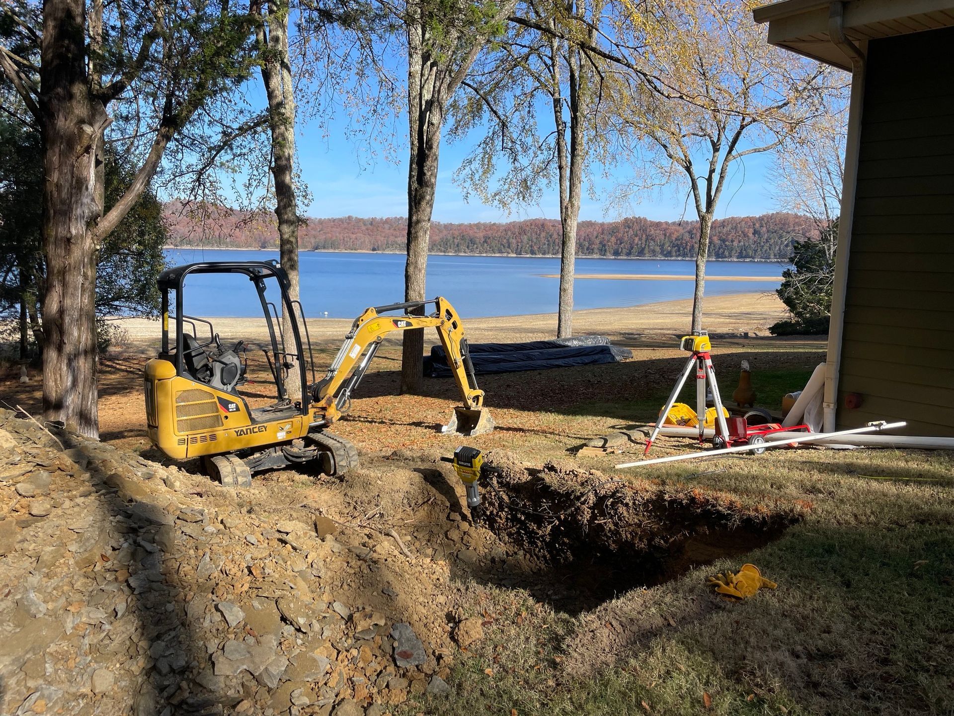 A yellow excavator is digging a hole in the ground in front of a house.