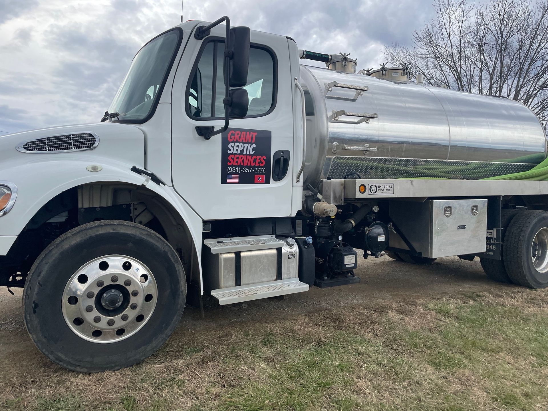 A white tanker truck is parked in a grassy field.