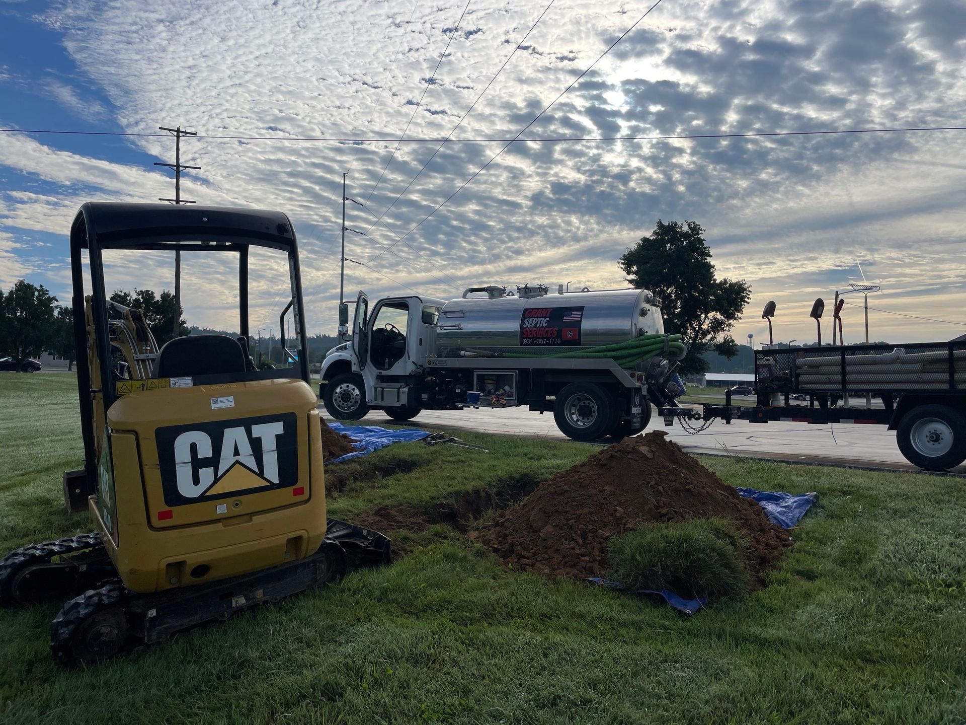 A cat excavator is parked next to a tanker truck.