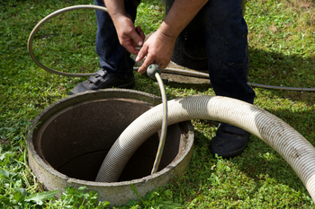 A man is pumping water into a septic tank with a hose.