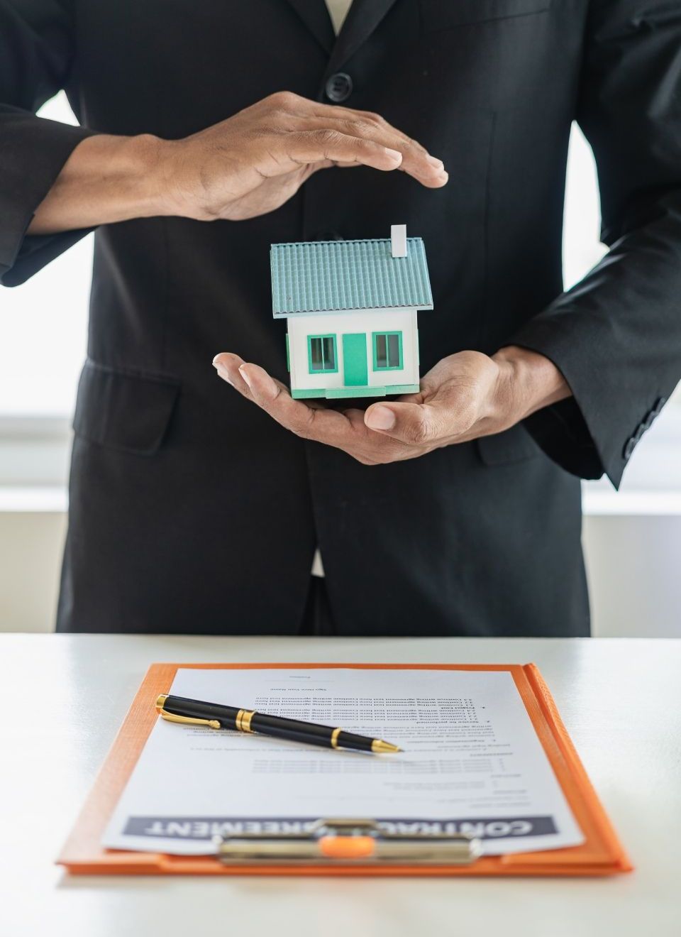 A man in a suit is holding a small house in his hands.