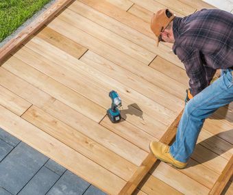 A man is working on a wooden deck with a drill.