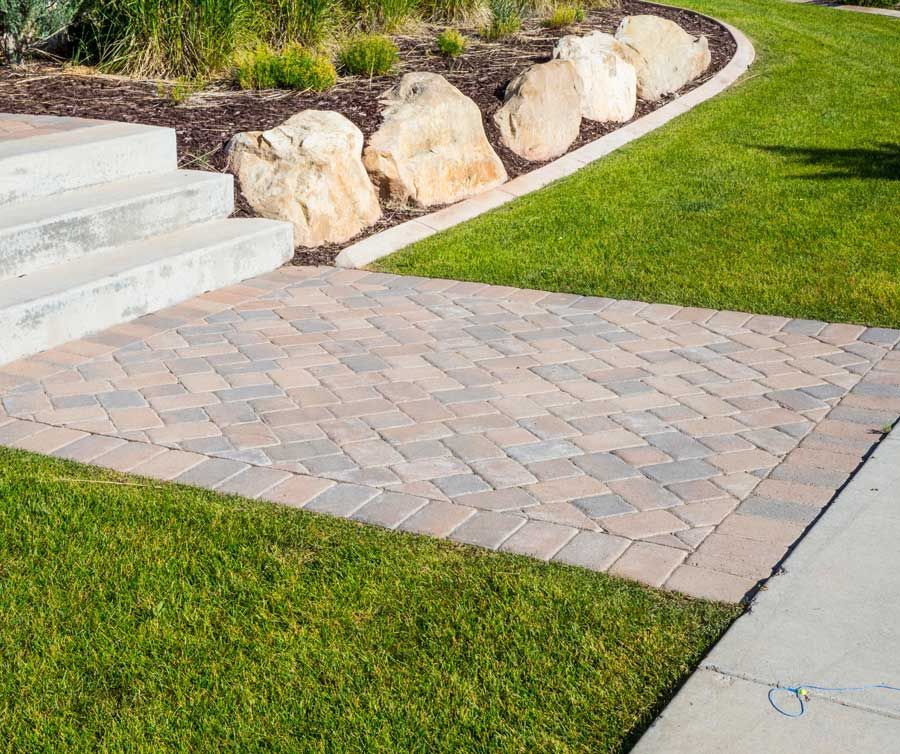 A brick walkway leading to a set of stairs and a lush green lawn.