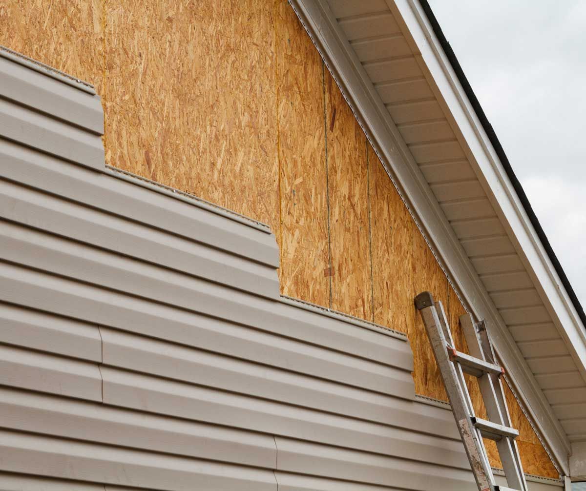A ladder is leaning against the side of a house with siding.