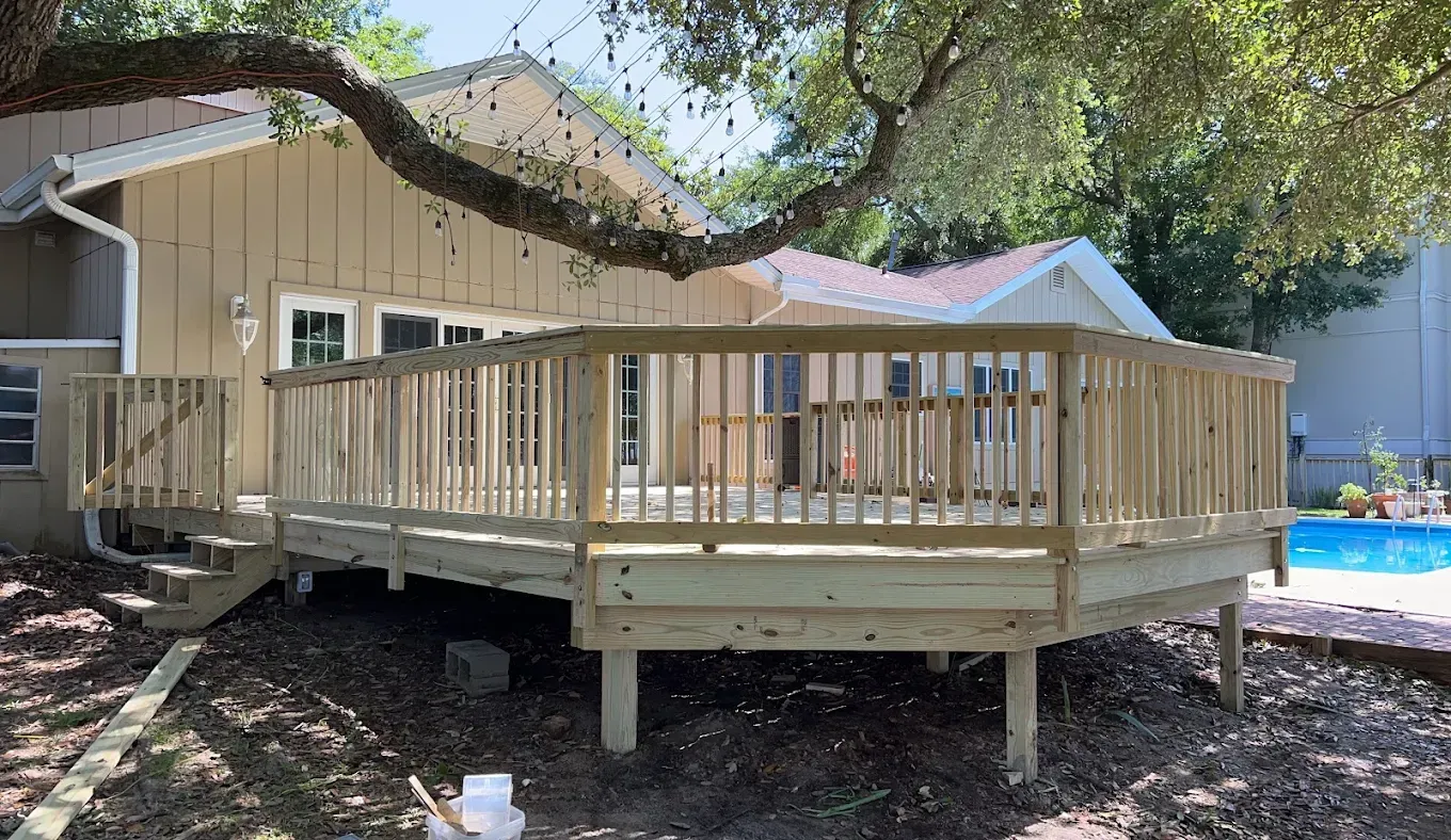 A wooden deck is sitting in front of a house next to a pool.