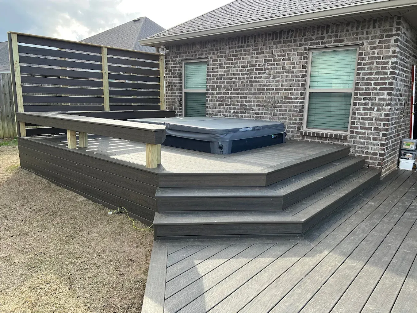 A deck with stairs and a hot tub in front of a brick house.