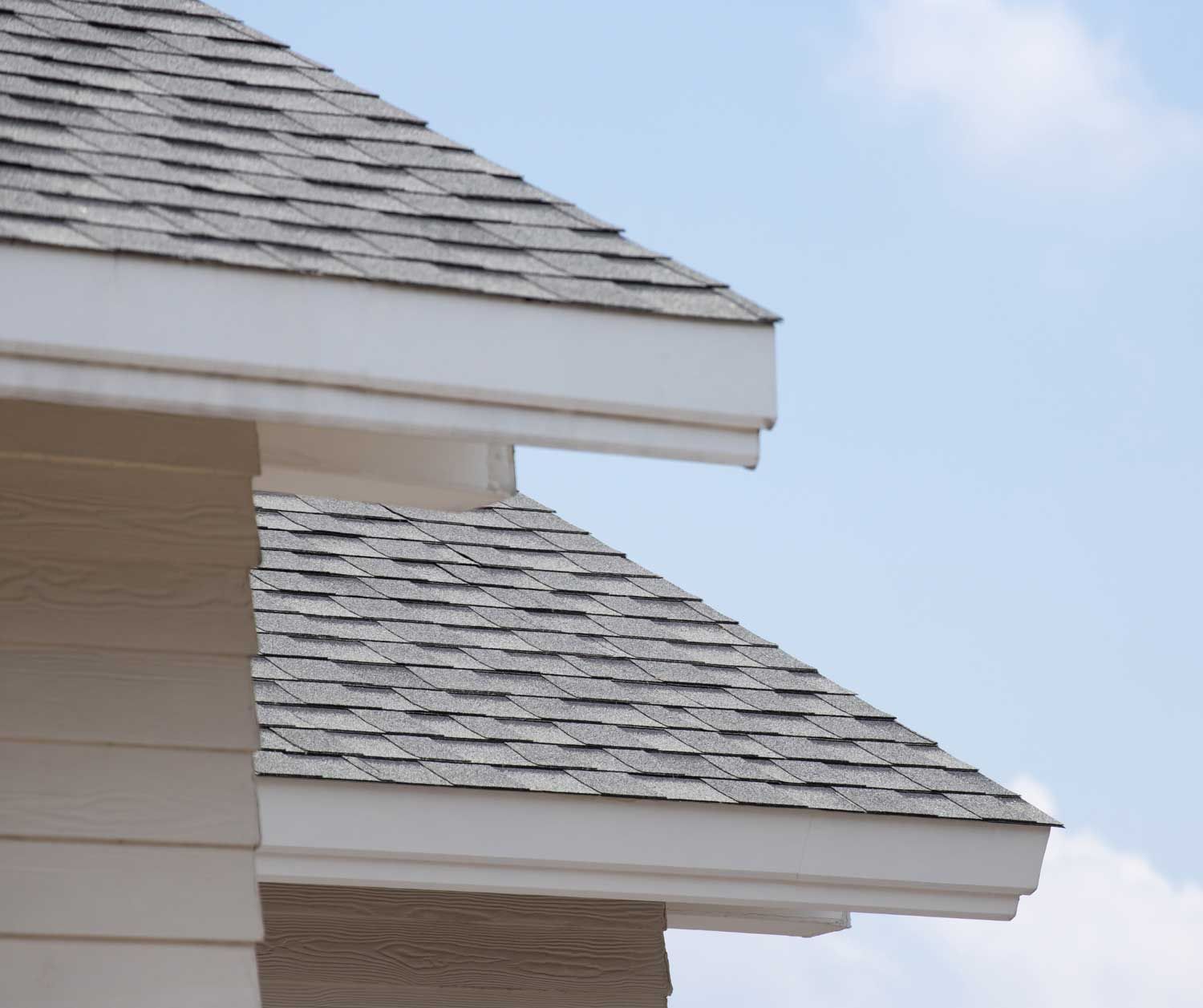 A close up of a shingle roof with a blue sky in the background