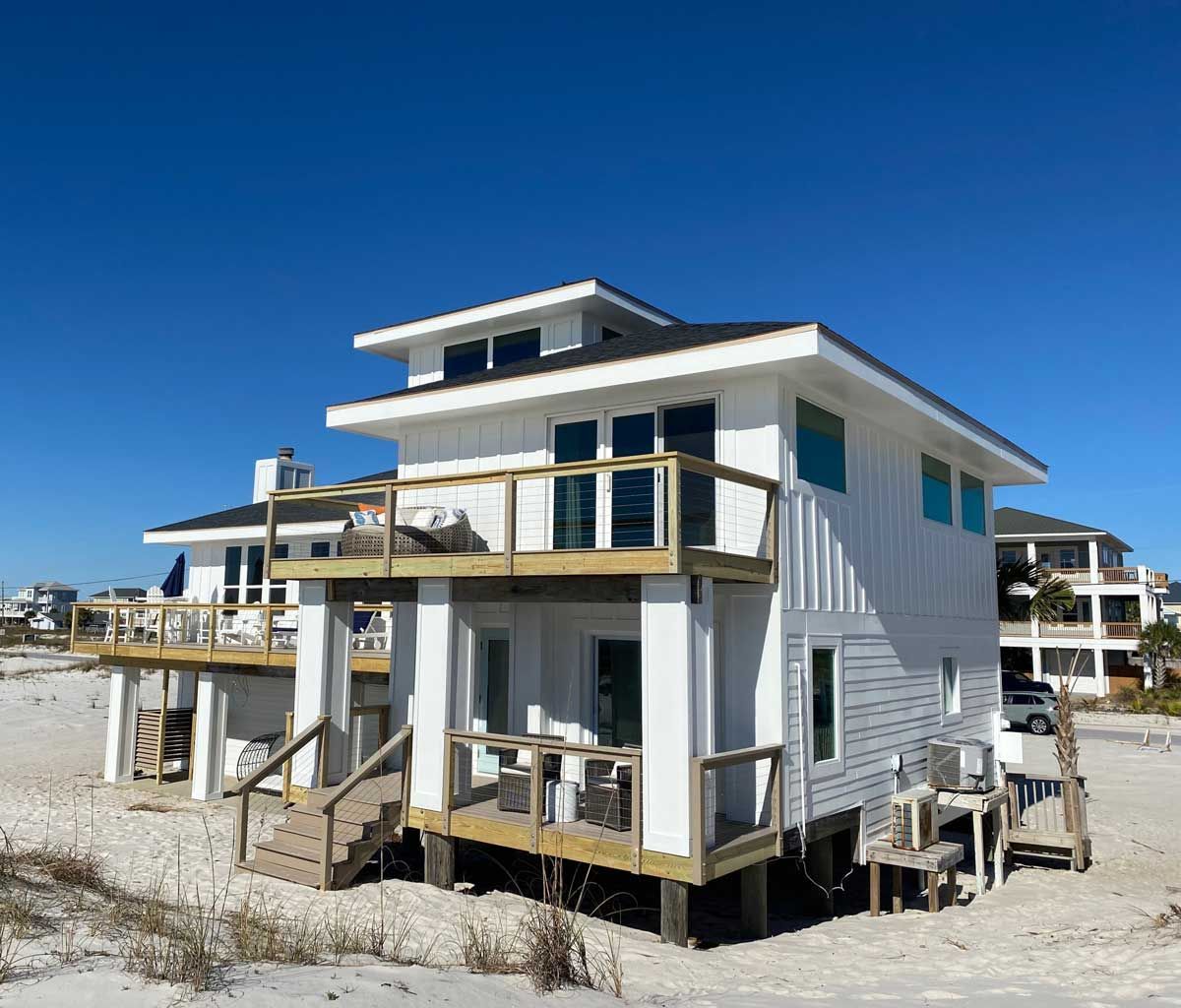 A white house with a wooden deck on the beach.