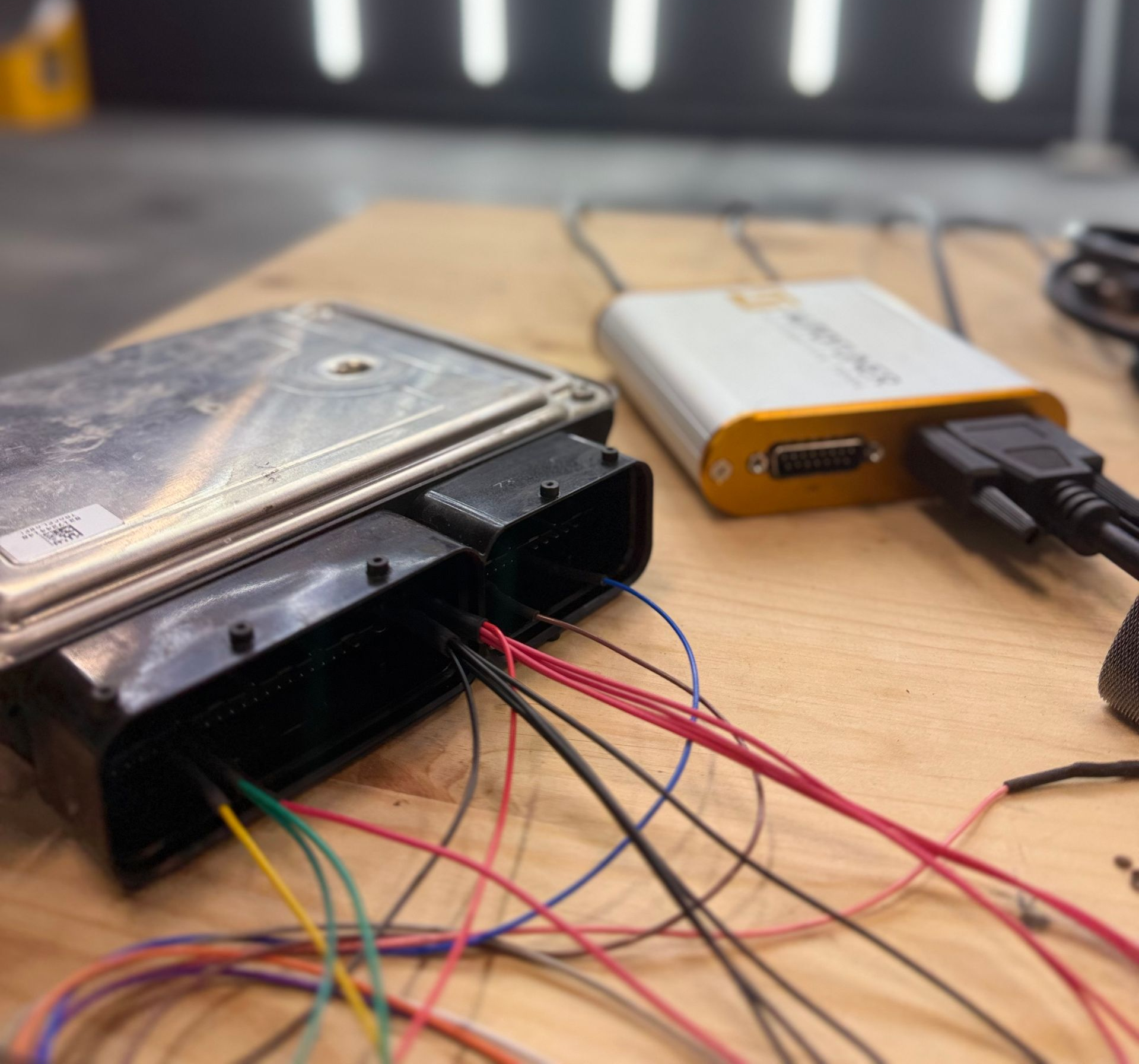 ECU connected to a programming device with colored wires on a wooden surface, likely for engine tuning.