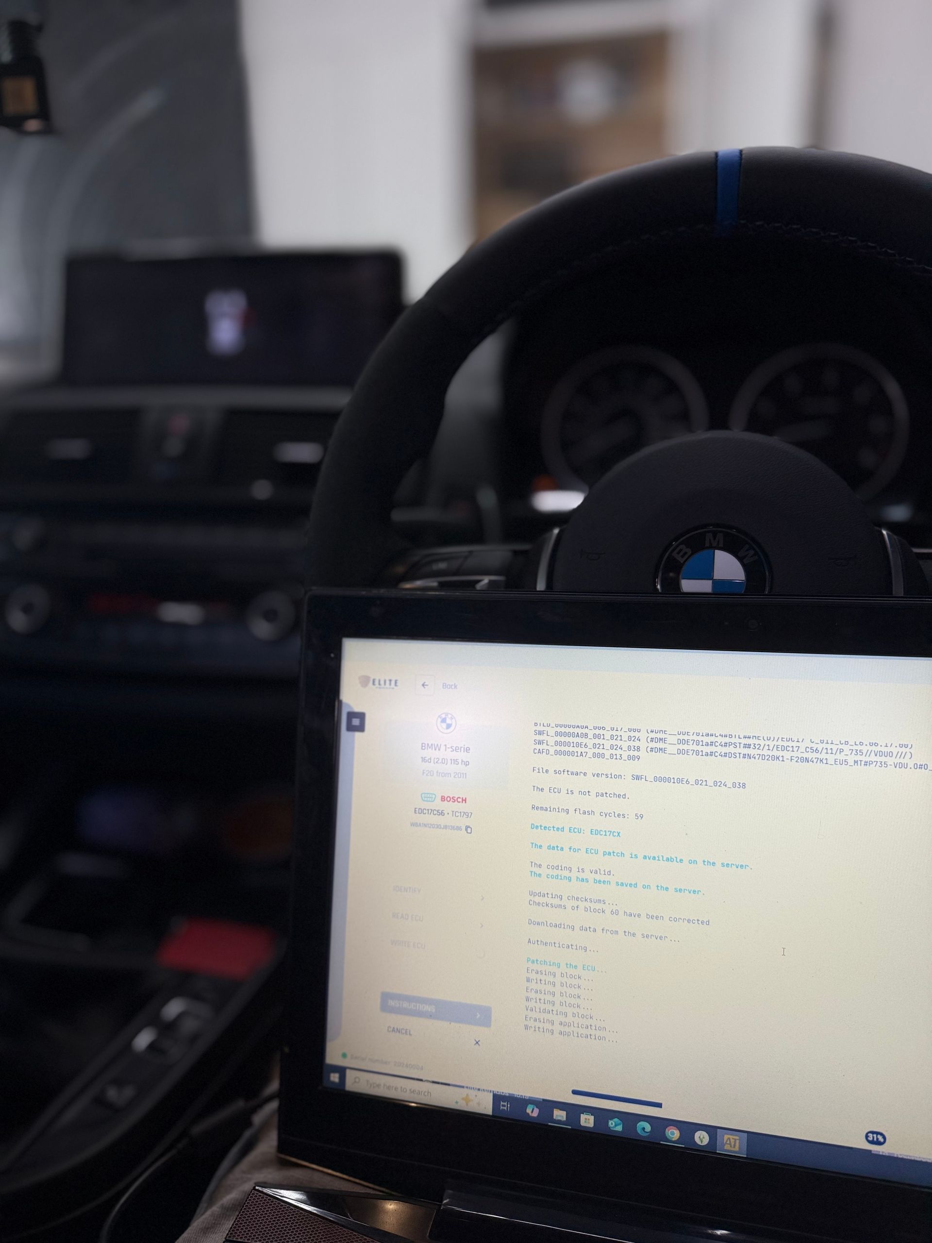 Laptop displaying code, inside a BMW. Steering wheel and dashboard visible.