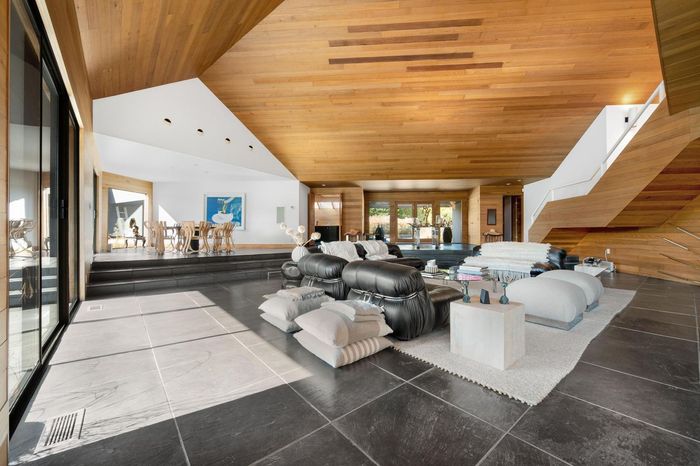 Spacious modern living room with wood ceiling, dark tiled floor, white sofas, and large windows.