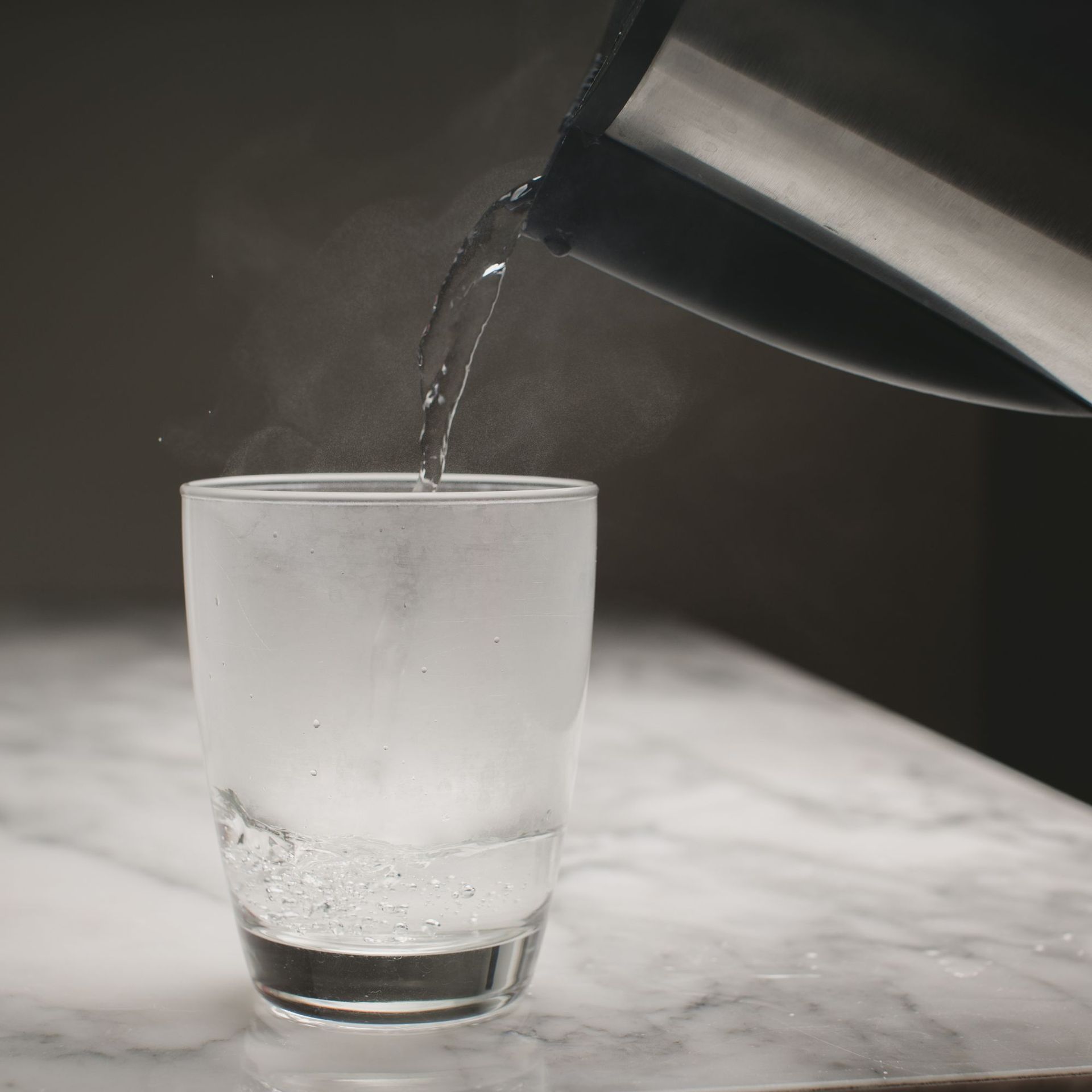 A glass of water is being poured from a kettle into a glass.