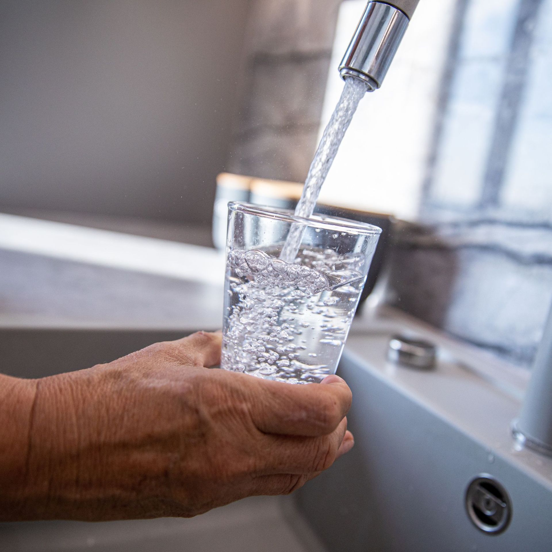 Tetra Water - A person is pouring water into a glass from a faucet.