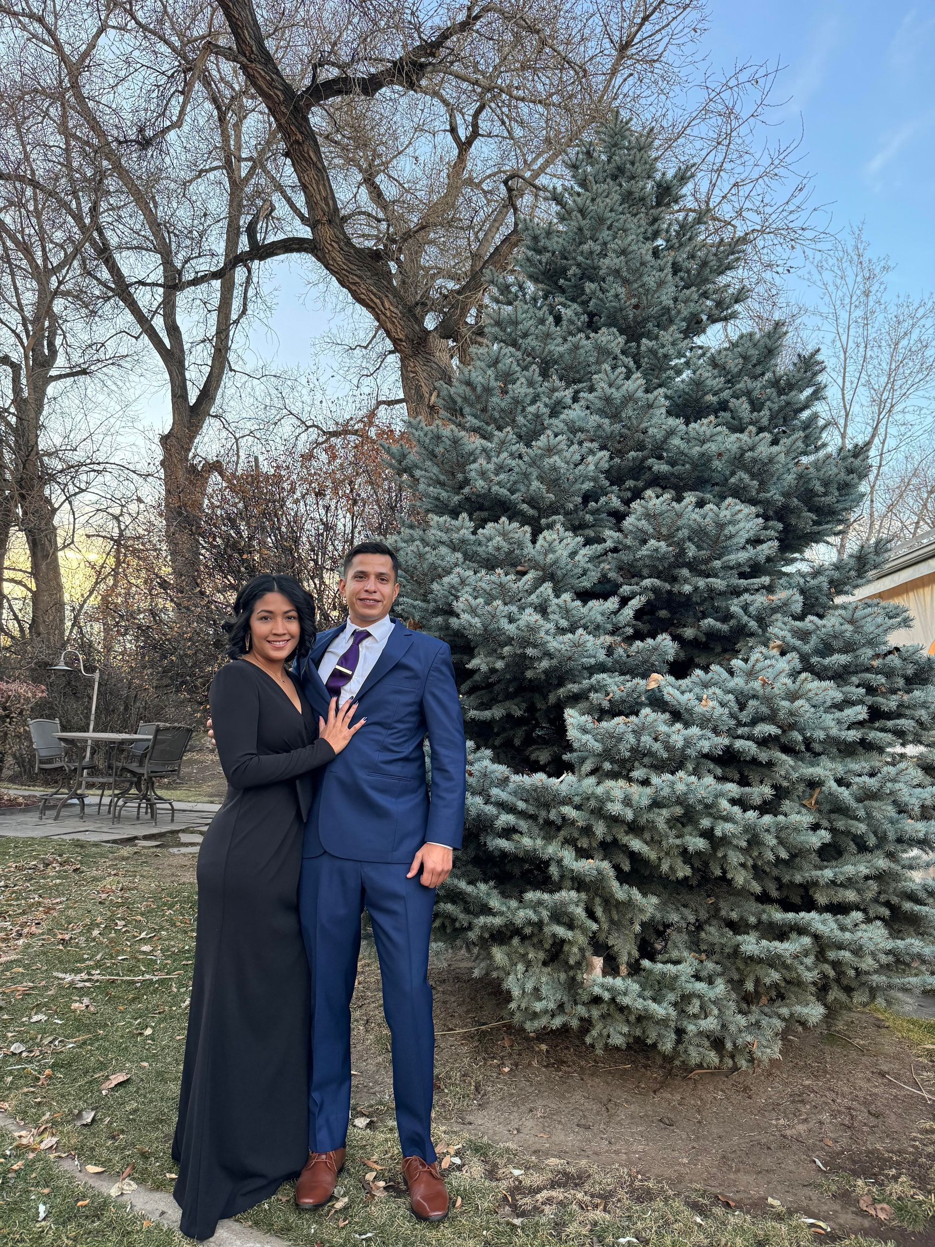 Man with tattoos sits on a bench in a park, hands clasped, looking at the camera.