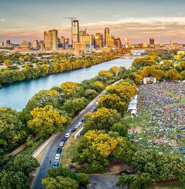 An aerial view of a river surrounded by trees with a city in the background.