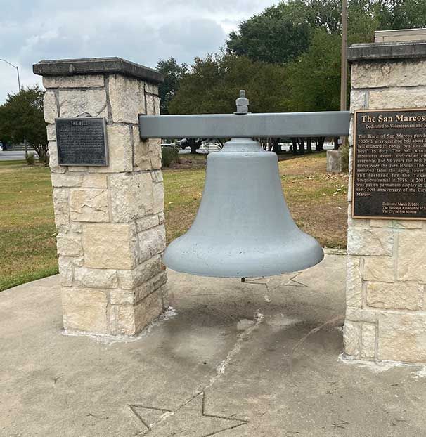 A large bell is hanging from a stone pillar in a park