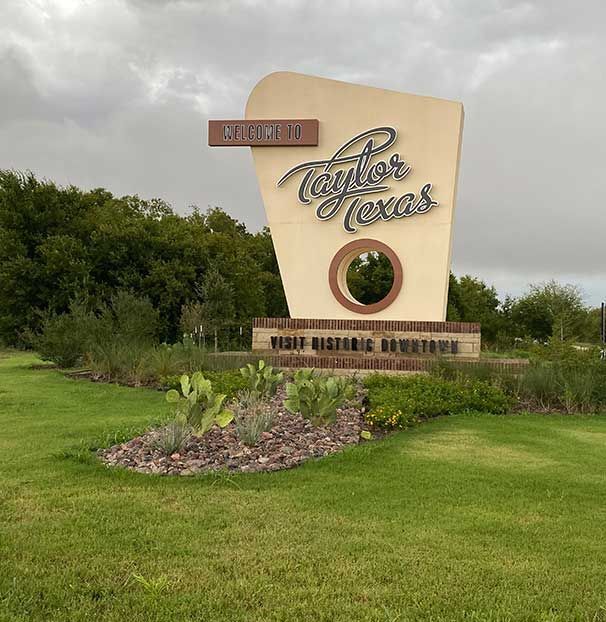A sign for taylor texas is in the middle of a lush green field