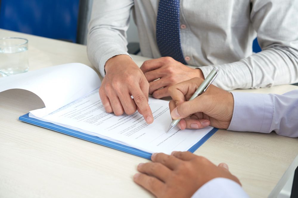 Hands of two people signing a document, one pointing at the signature line.