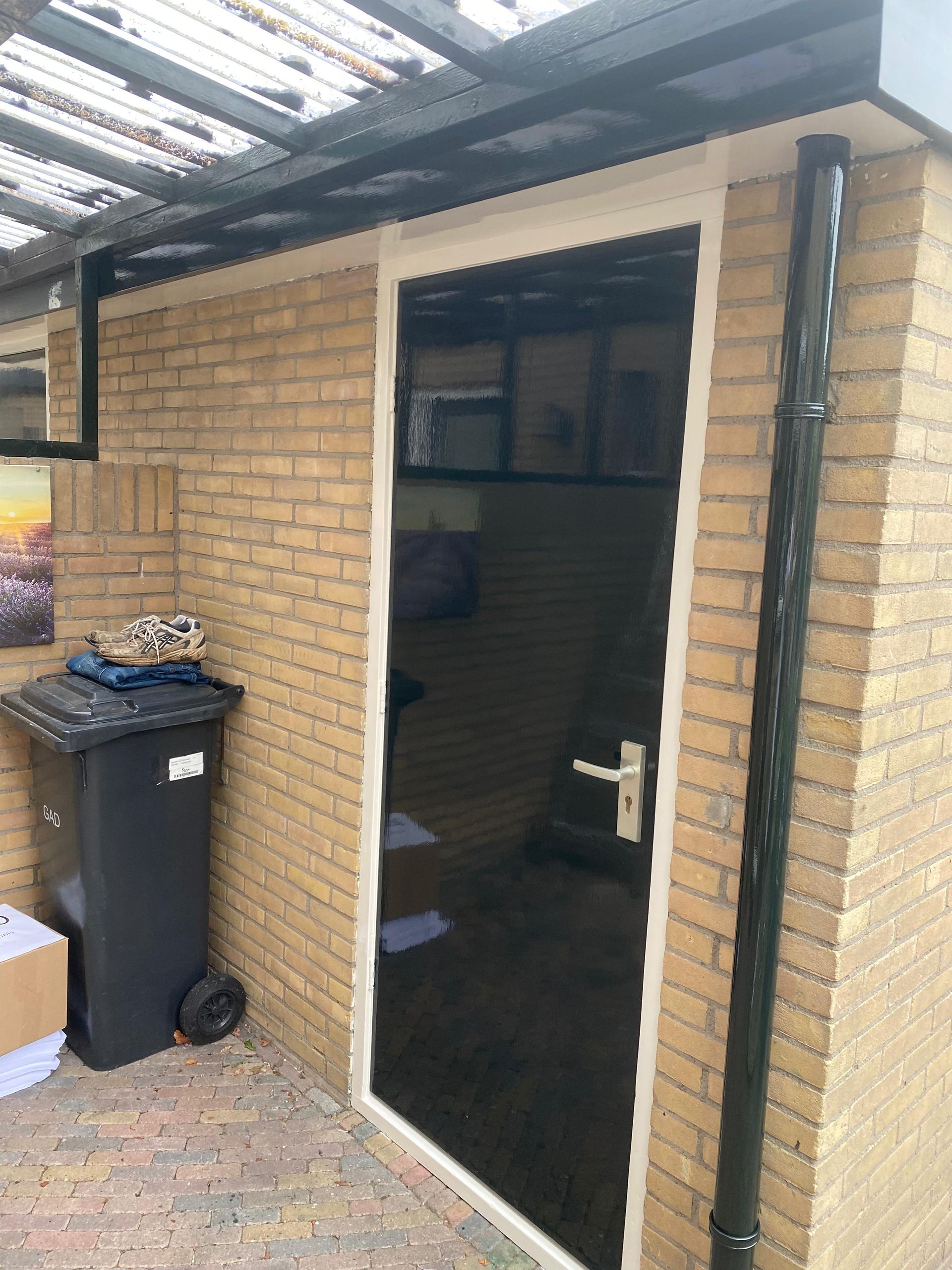 Een zwarte deur zit op een bakstenen muur naast een vuilnisbak.