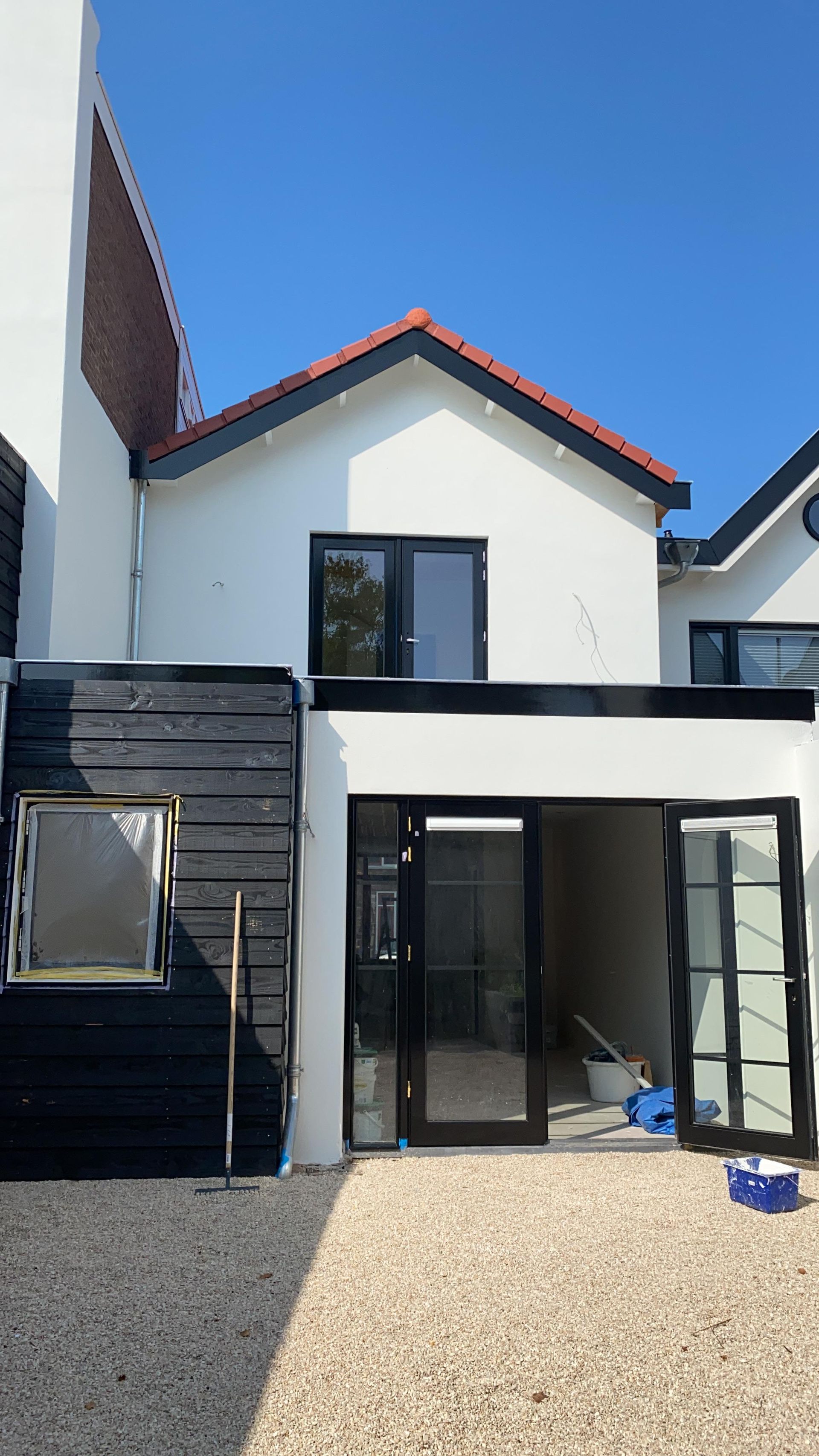 Er wordt een wit huis gebouwd met zwarte ramen en een rood dak.