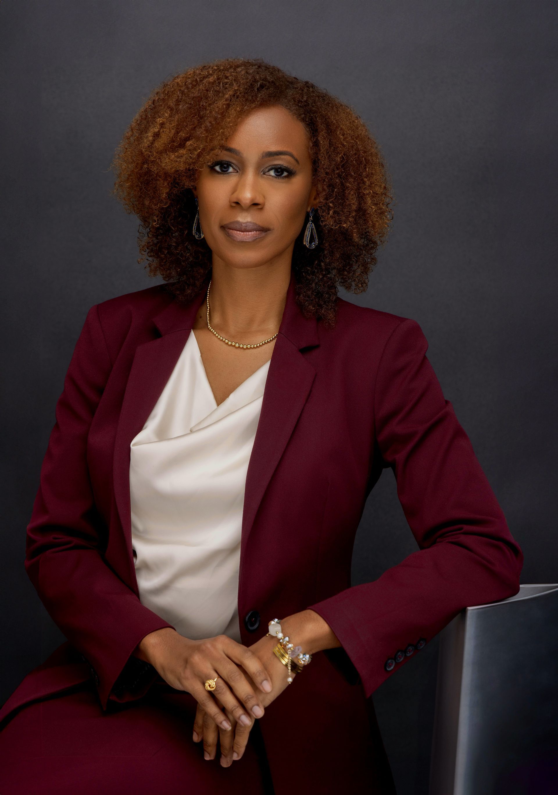 A woman in a black jacket is smiling in front of a brick wall.