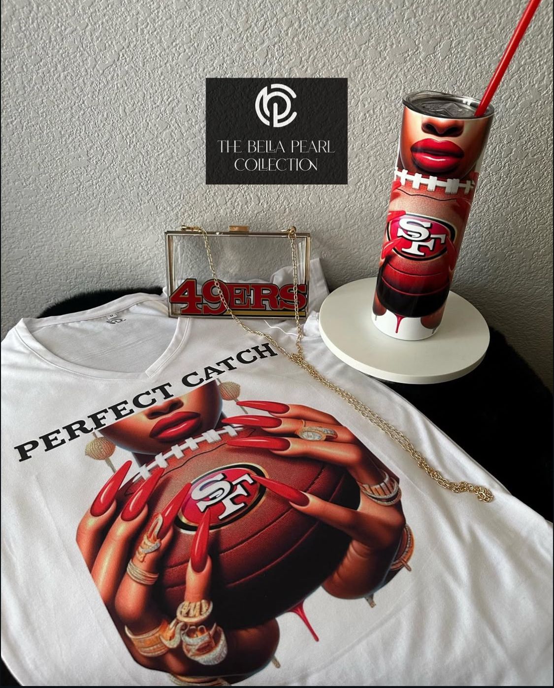 Collection of 49ers-themed merchandise: shirt, tumbler, purse, and chain, against a textured background.
