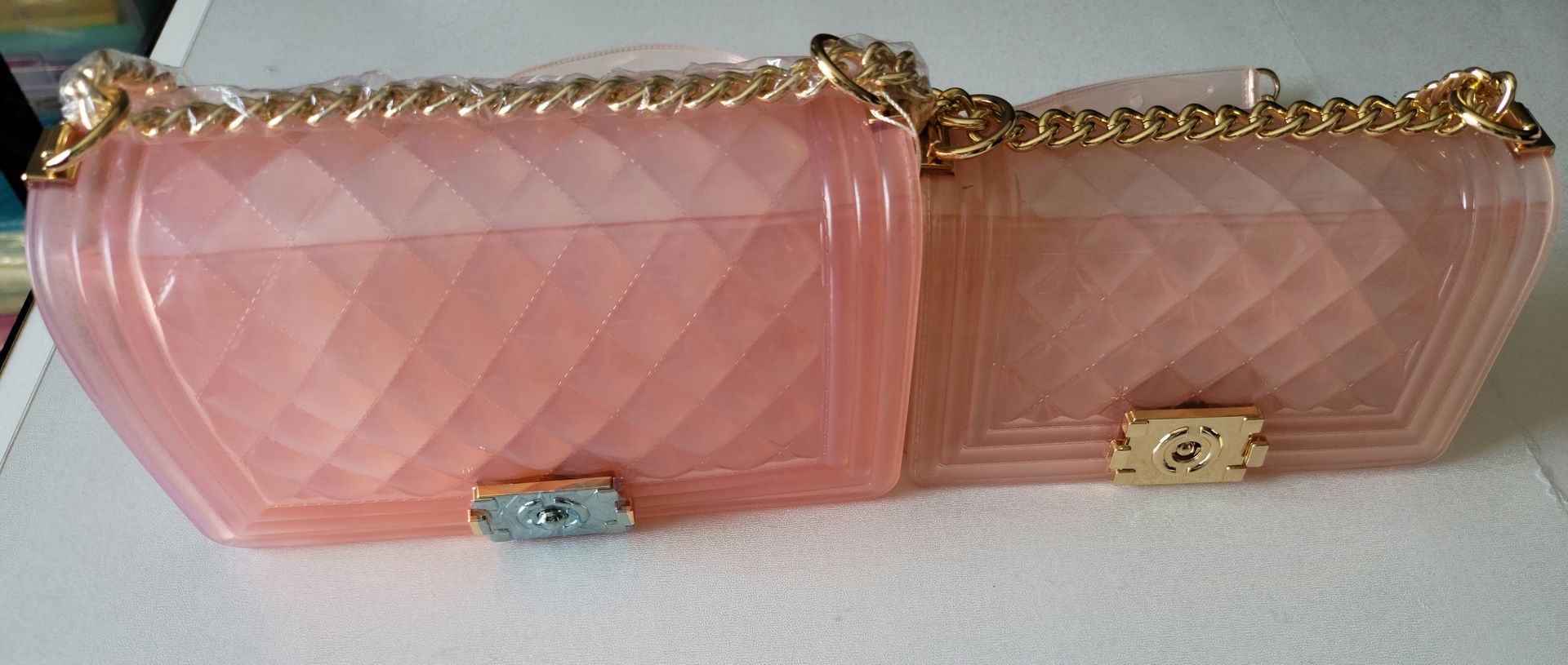 Two pink handbags with gold chains are sitting on a table.