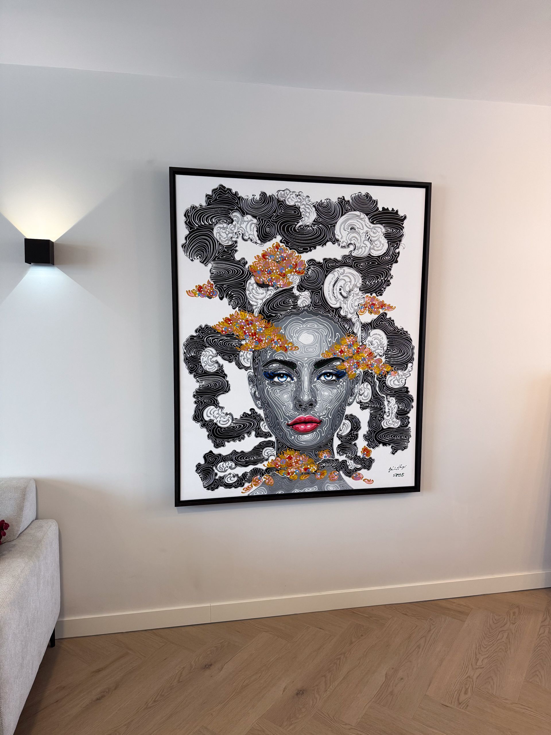 Kunstwerk van een vrouwengezicht, met zwarte en gouden accenten, ingelijst op een witte muur.