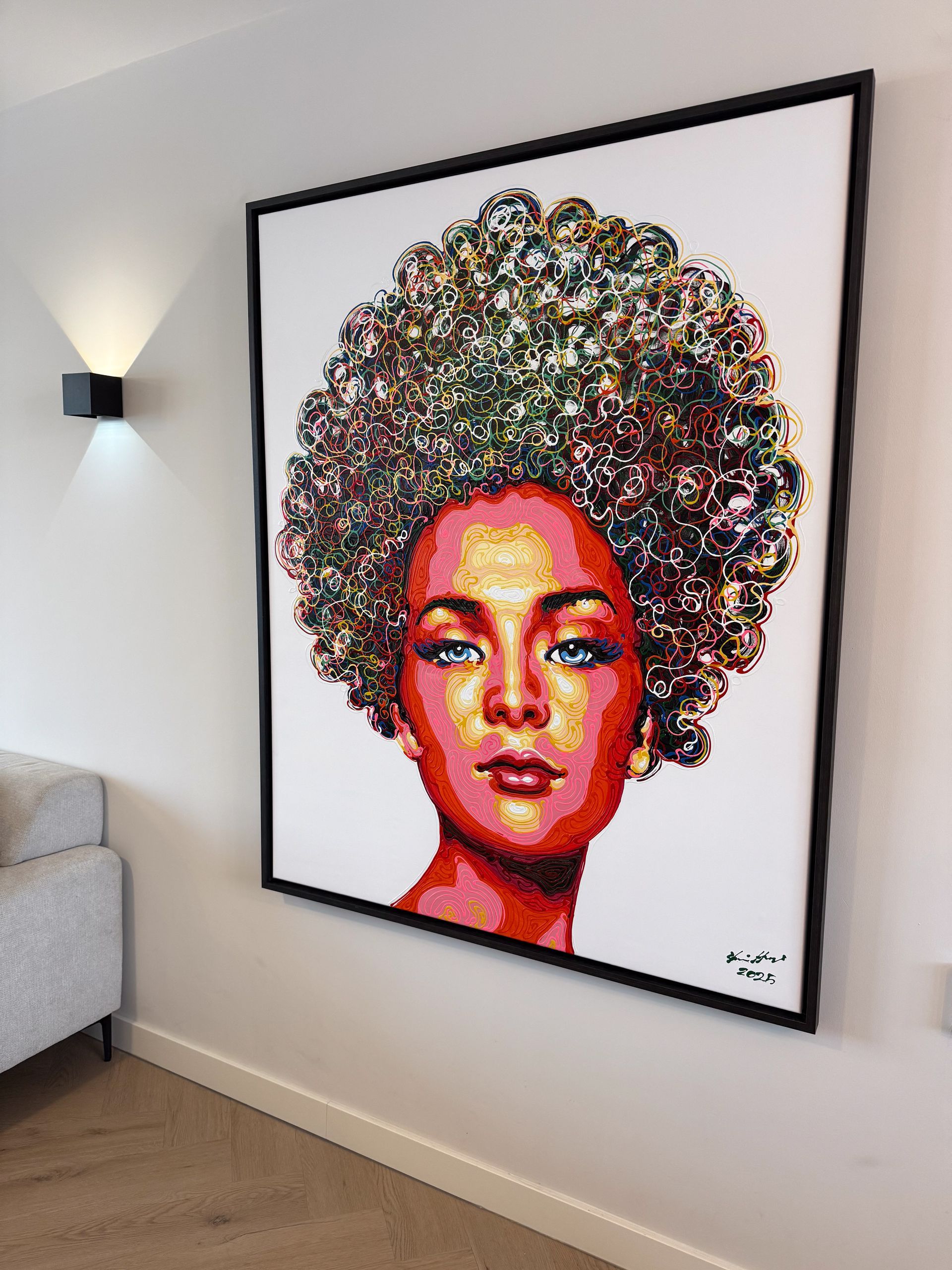 Portretschilderij van een vrouw met een kleurrijke afro, op een witte muur, met een zwarte lijst. Zwarte wandlamp.