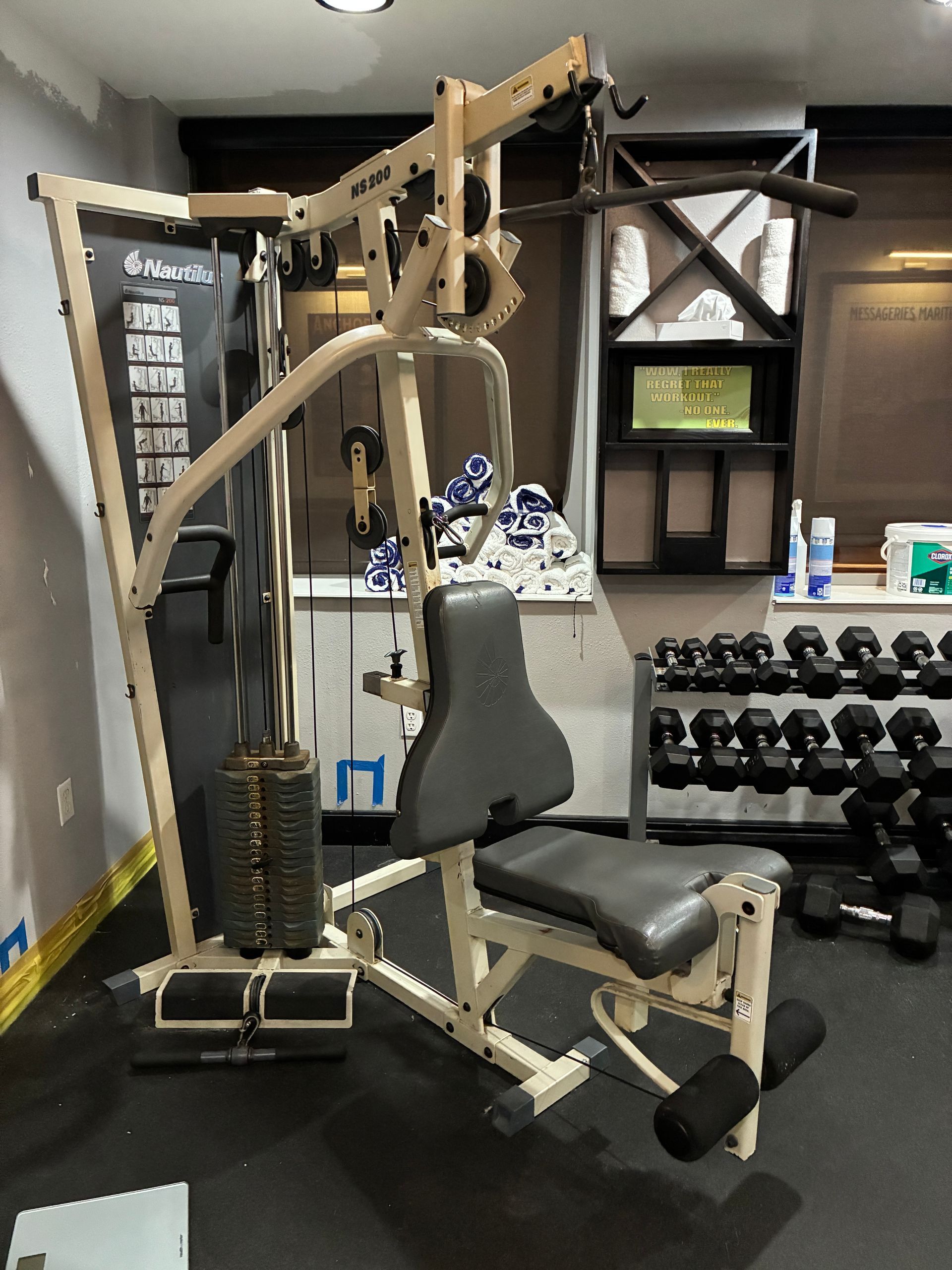 Tan multi-station home gym with weight stack, seated bench, and pulldown bar in a home gym.