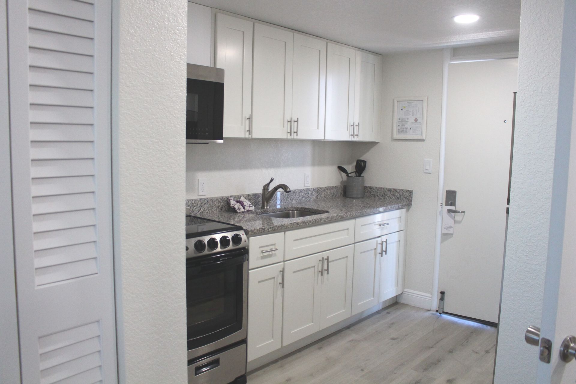 A small, white kitchen with a microwave, cabinets, a stove, and a doorway.