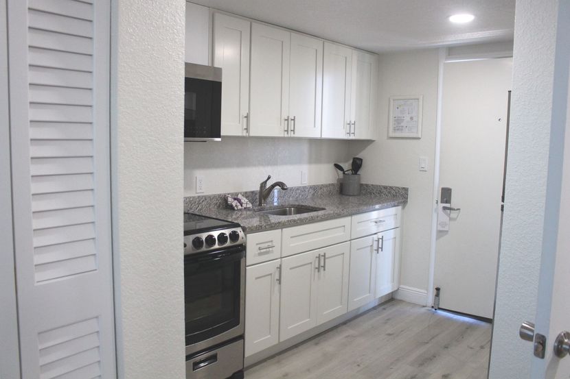 A small, white kitchen with a microwave, cabinets, a stove, and a doorway.