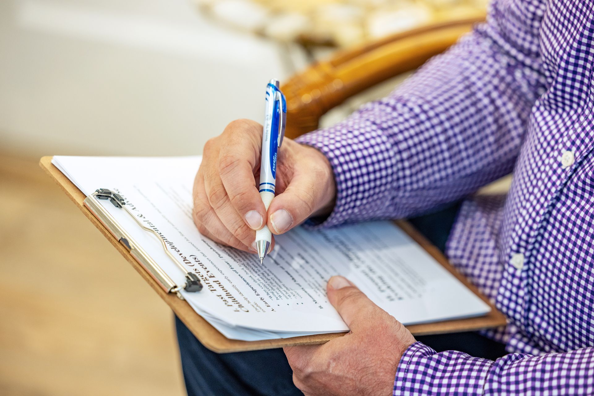 A person with head in hands sits in therapy. A counselor has hands clasped in front of them, holding a clipboard.