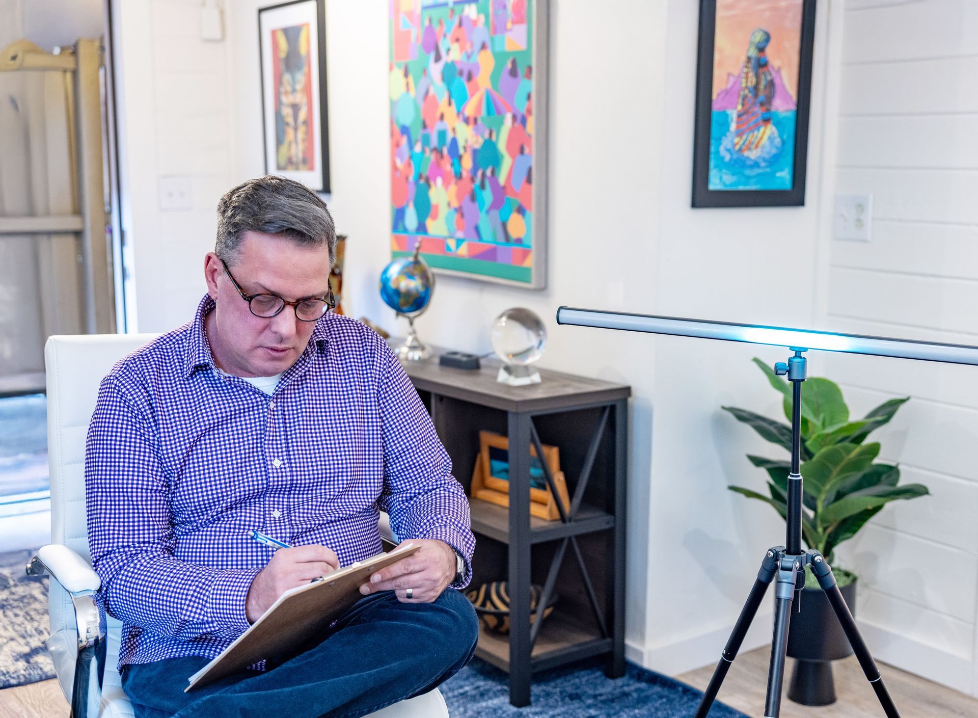 Man in therapy session, looking up with a pensive expression while a person holds a clipboard and pen.