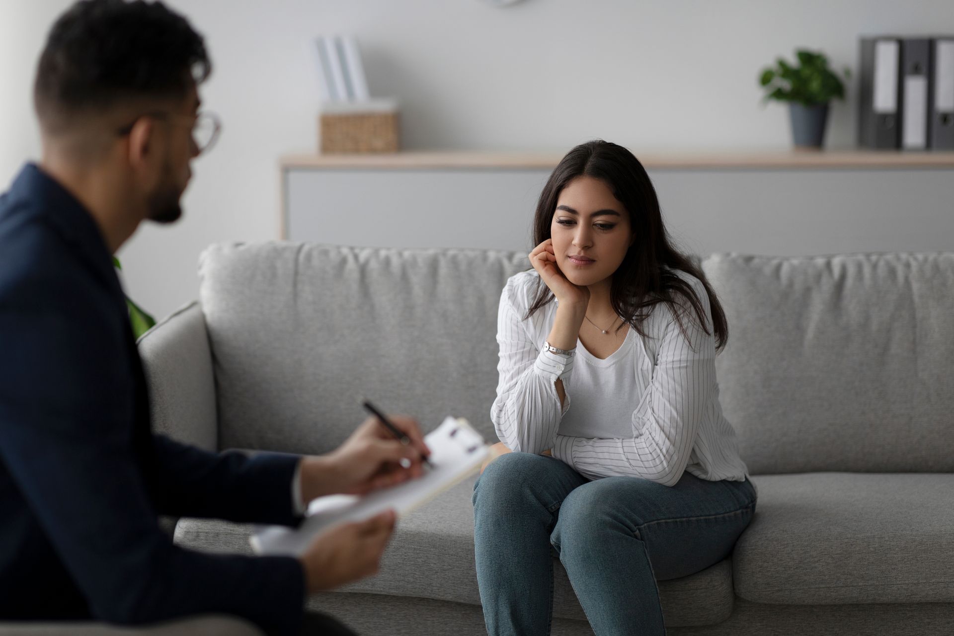 Therapist taking notes during a session with a woman on a couch.